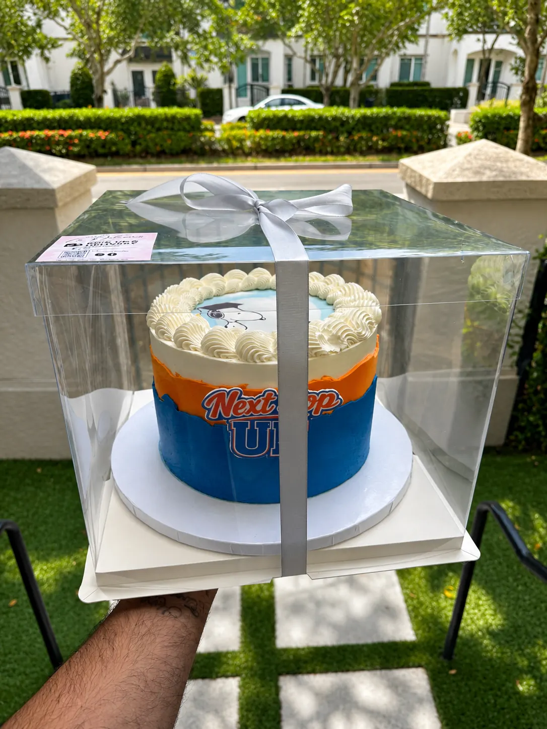 Torta azul y naranja estilo universitario dentro de caja transparente.
