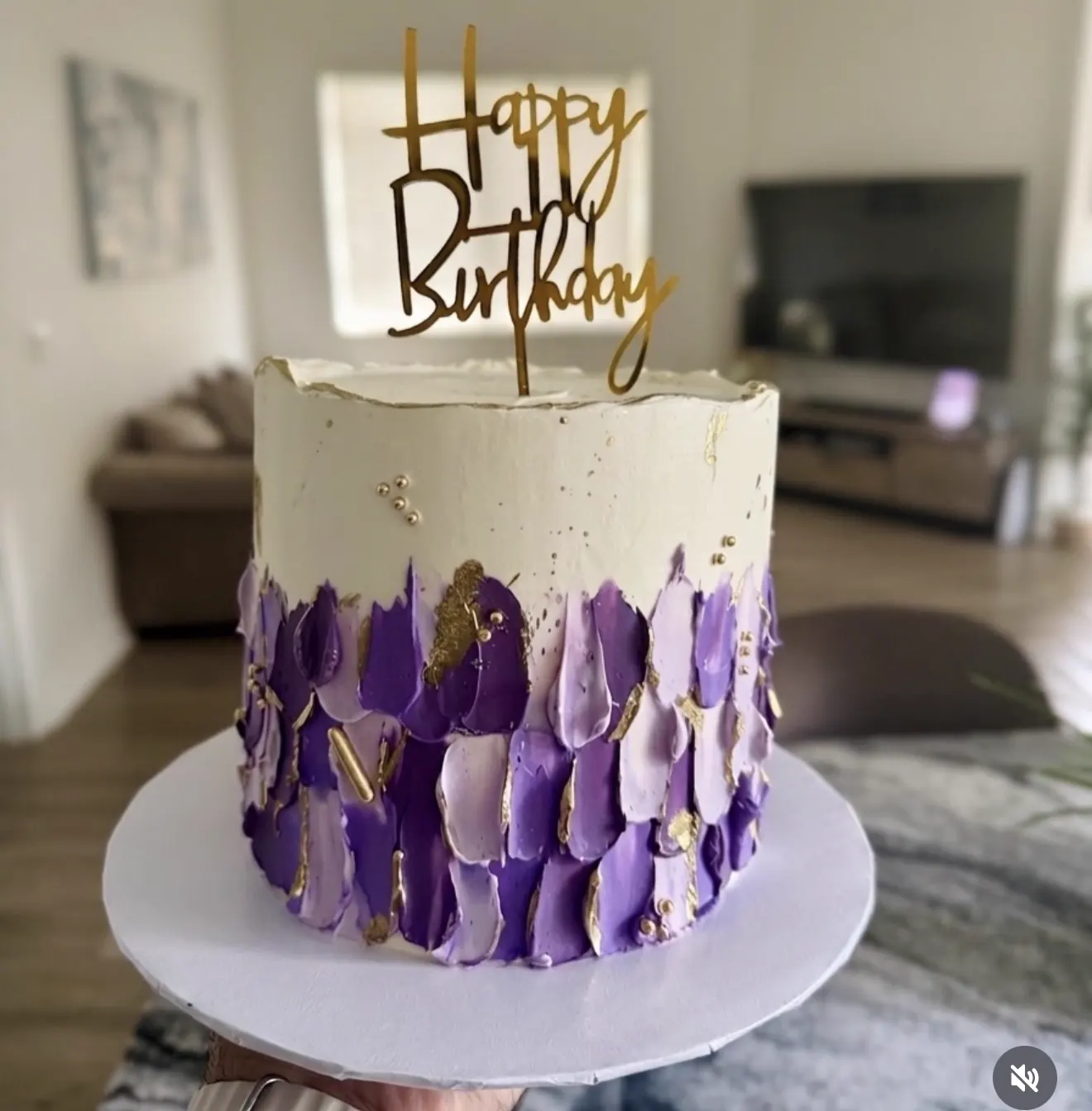 Torta blanca con pinceladas moradas, detalles dorados y topper Happy Birthday.